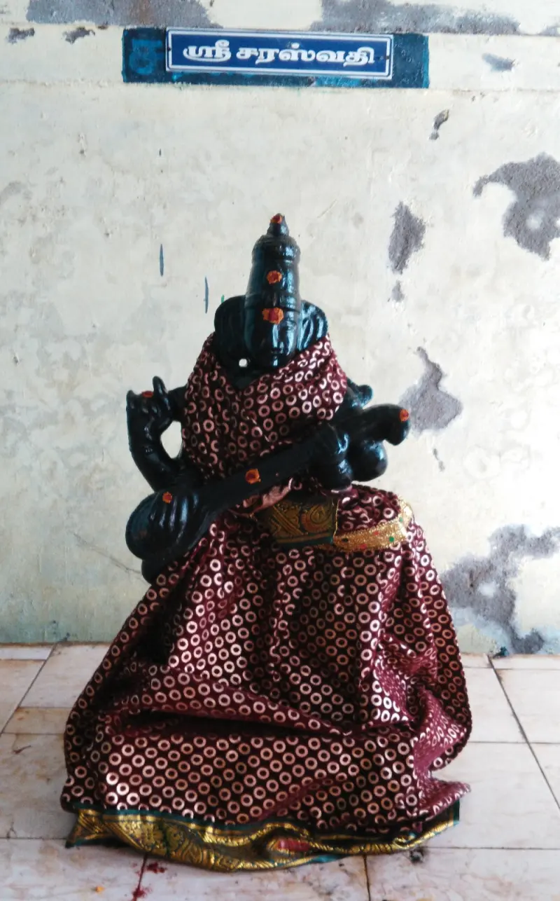 Black Sarasvathi idol holding a veena, dressed in a maroon and gold sari