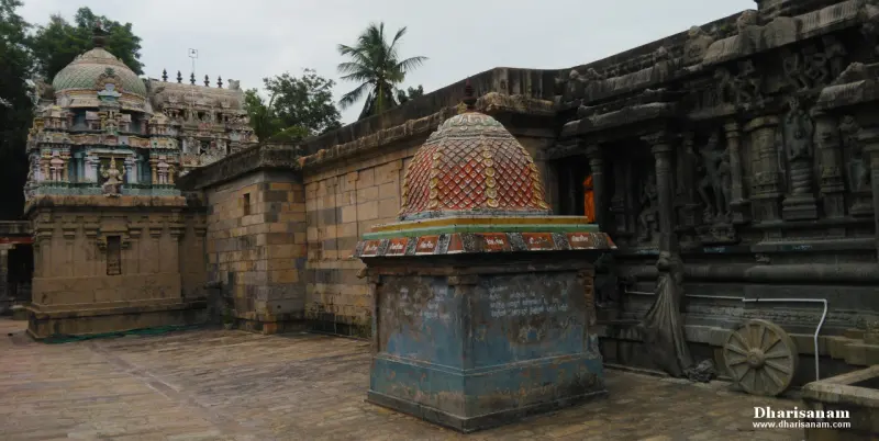 A blue pedestal with a domed top in the courtyard, with the carved sanctum wall and a stone wheel at right.
