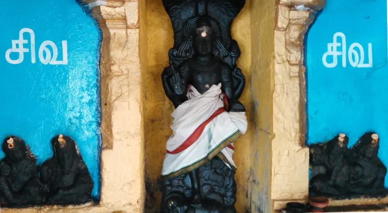 A standing black stone figure in a white cloth, with two small seated figures at each side.