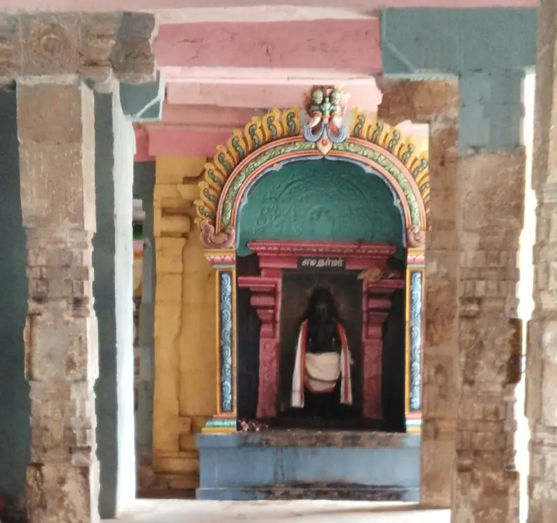 A painted arch frames a small shrine with a dark idol, seen between stone pillars of the corridor.