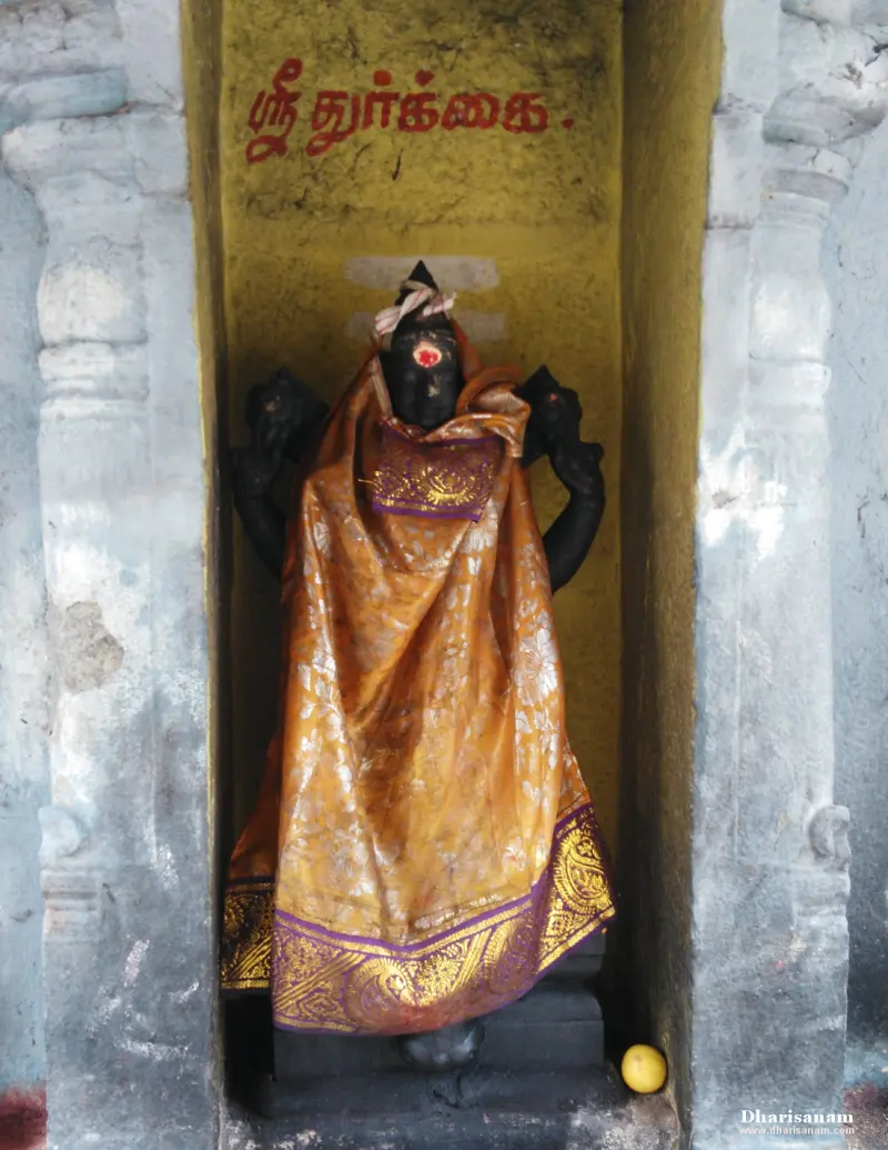 A dark stone idol dressed in an orange silk cloth in a niche, with Sri Durgai written above in red