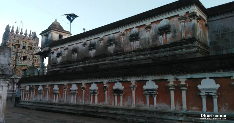 A long wall painted red and white with rows of decorative pilasters, with the gopuram at far left