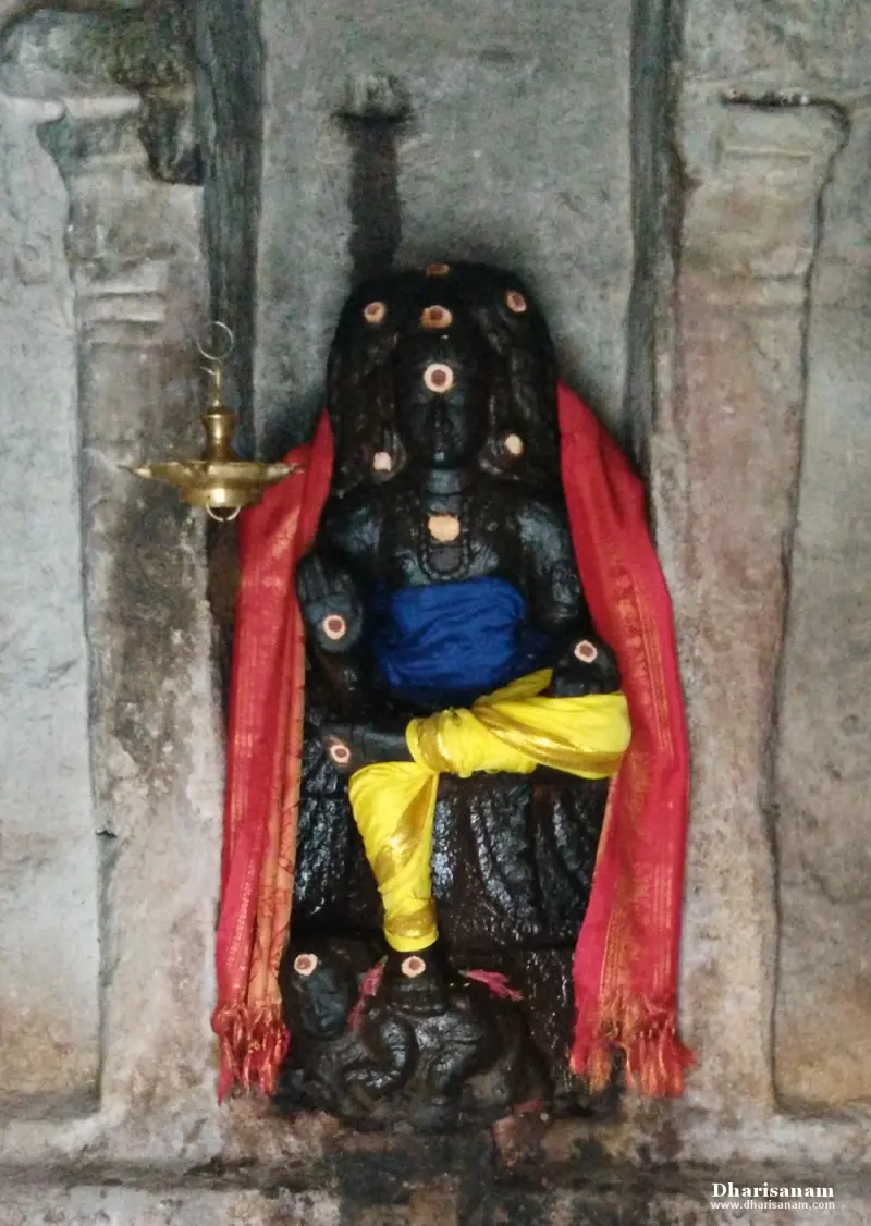 A seated dark stone idol with a red cloth over its shoulders and yellow cloth at the waist, in a niche