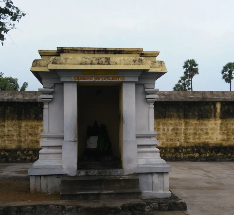 A small open shrine on a stone base with a name board for Lakshmi Narayanar and two figures inside.