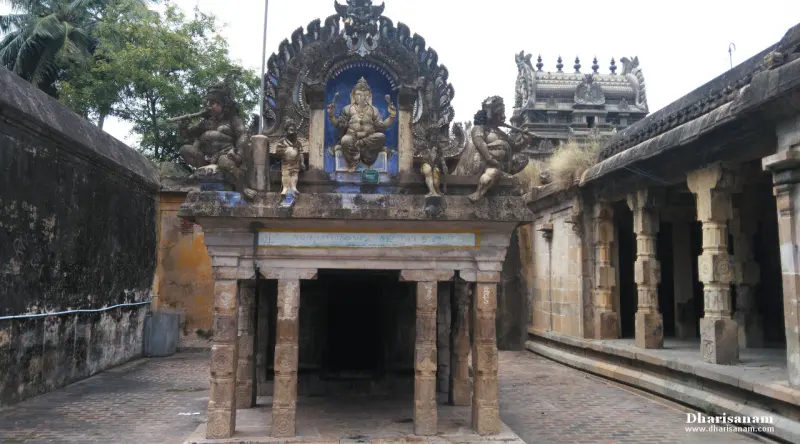 A small pillared shrine topped by a seated Ganesha figure with musicians, beside a long colonnade