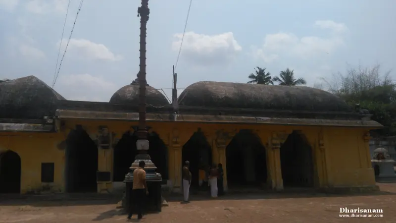 Tall flag post before a yellow arched hall with domed roofs, and a few people