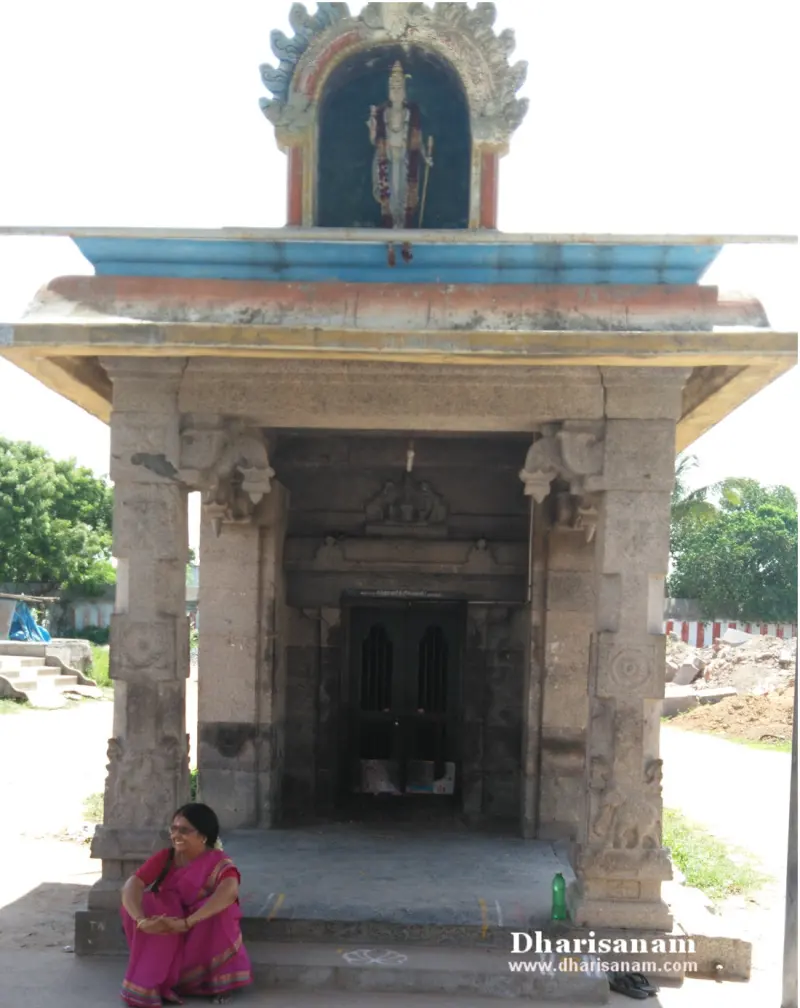 Stone shrine with pillars and a closed door, a painted figure above and a person sitting in front
