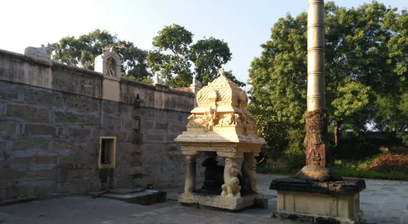 A small Nandhi pavilion beside a tall golden flagstaff by the wall