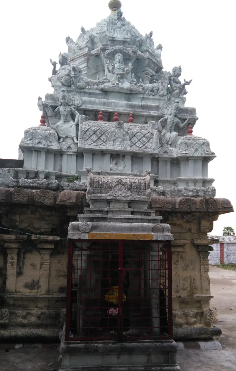 A tiered stone tower decorated with sculpted figures, above a small shrine behind a red iron grille.