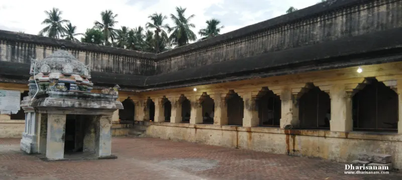 A long corridor of arched openings along a paved courtyard, with a small shrine on the left.