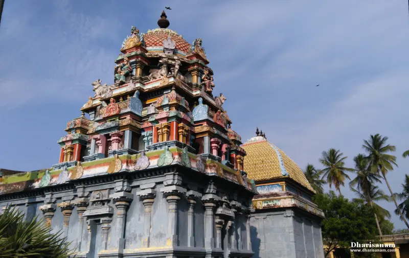 A tiered colourful tower with carved figures and a golden-yellow dome beside it, palm trees behind