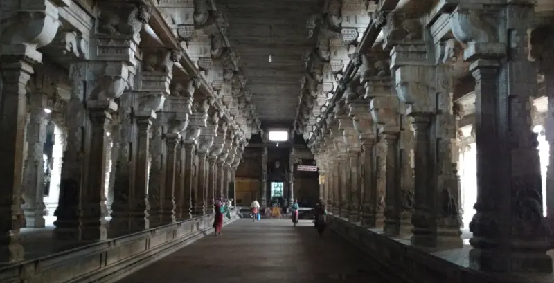 A long hall with rows of carved stone pillars on both sides and a few people far down the aisle.