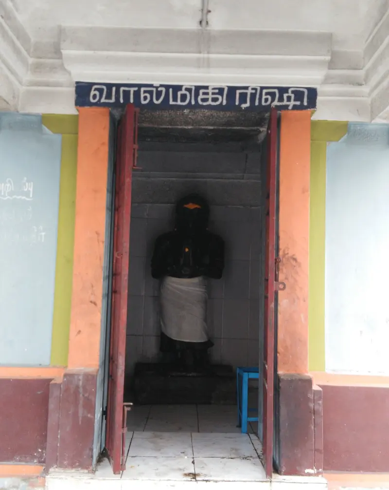 Black standing figure in white cloth inside a small shrine with a blue name board