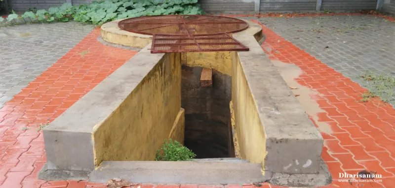 Stone-walled well with a metal grille, on red paving
