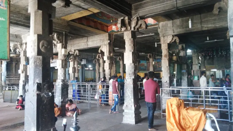 Stone pillared hall with steel railings and devotees standing and sitting