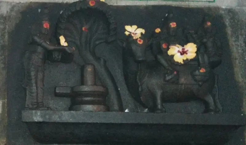 Dark stone relief of a lingam under a serpent hood, with a standing figure and a bull with riders.