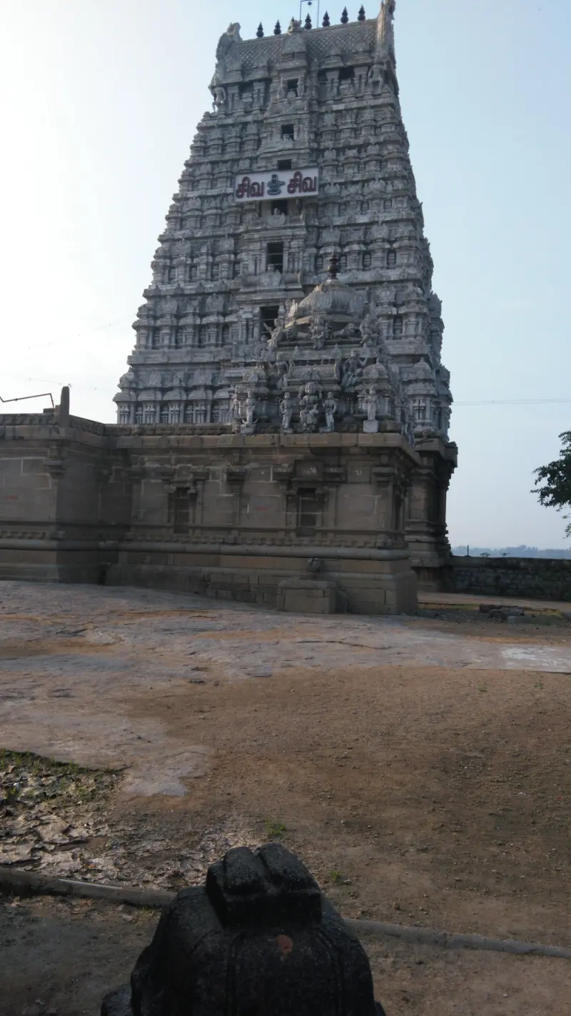 A tiered gopuram behind a bare rocky courtyard, with a black stone Nandi in the foreground