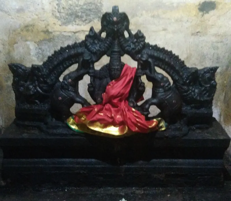 A dark stone figure between two elephants, draped in a red cloth