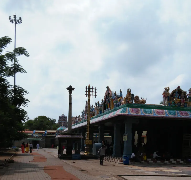 A mandapam roof lined with painted deity figures, with a stone pillar and a golden flagstaff in front.