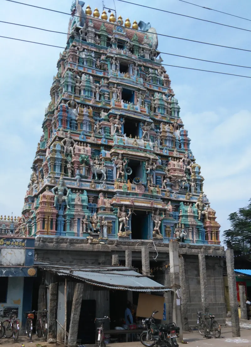 Tall colourful tower crowded with sculptures, above shops and bicycles