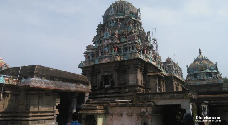 A stone temple building crowned by a tower with painted figures, a domed roof beside it at the right