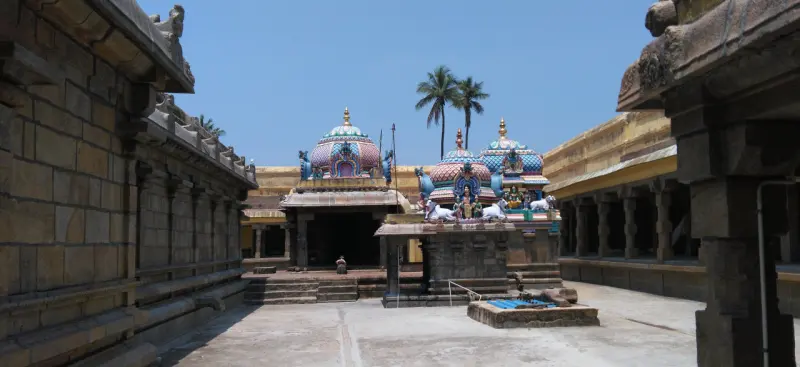 A paved courtyard between stone walls, with shrines topped by painted domes under a clear blue sky
