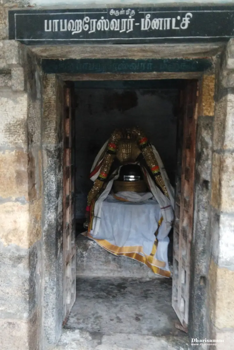 A small stone doorway with a Tamil name board; inside, a lingam dressed in white cloth and garlands.