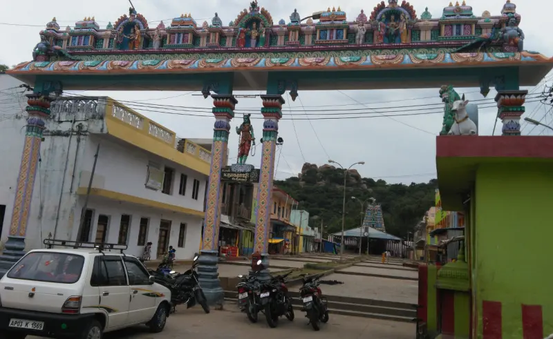 A road arch with painted figures on top, with a rocky wooded hill in the distance