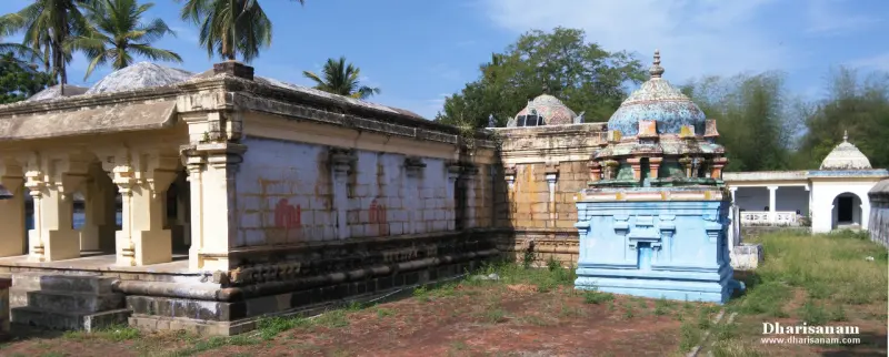 Pillared hall with a low roof beside a small blue shrine with a domed top, under palm trees