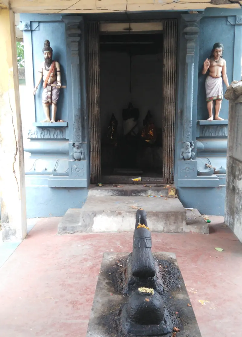 A blue doorway flanked by two standing figures, a Nandi and lingam before it