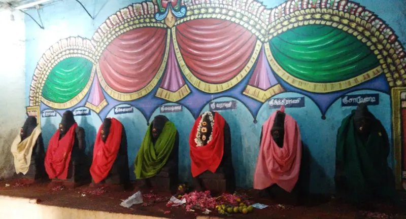 Seven black goddess statues in coloured cloths against a painted wall