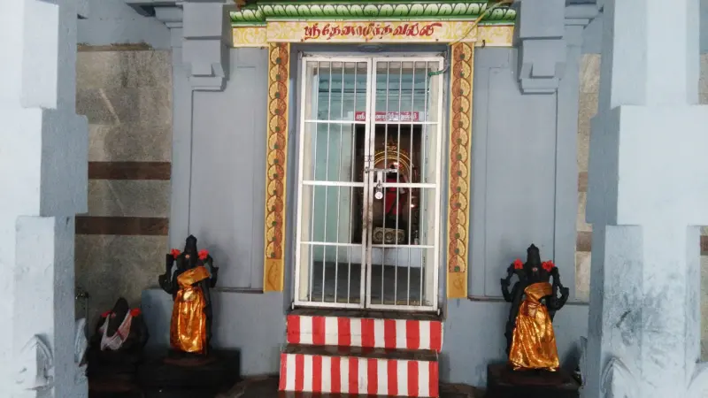 A grilled shrine doorway with red and white steps and a name board, guarded by two figures in gold cloth.
