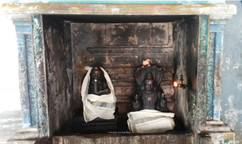 Two dark stone idols draped in white cloth sit inside a worn shrine niche, a lamp lit beside them