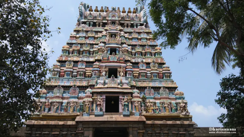 Tiered gopuram covered in sculpted figures, framed by trees and a palm
