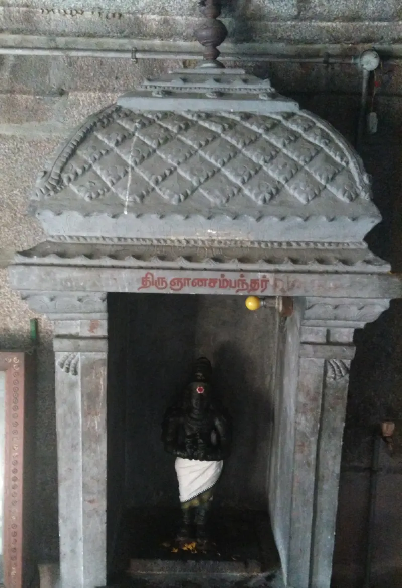 A small stone shrine with a quilted canopy and a dark idol in white cloth, name painted above