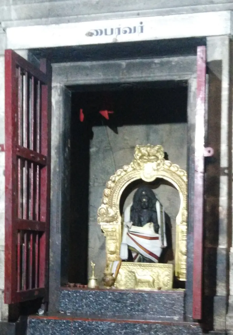 Dark Bairavar idol with white cloth under a gold arch