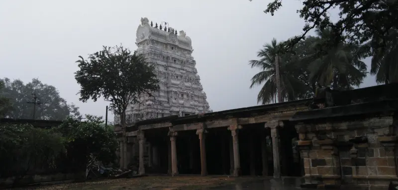 The tall temple tower rising behind a stone pillared hall under a grey sky.