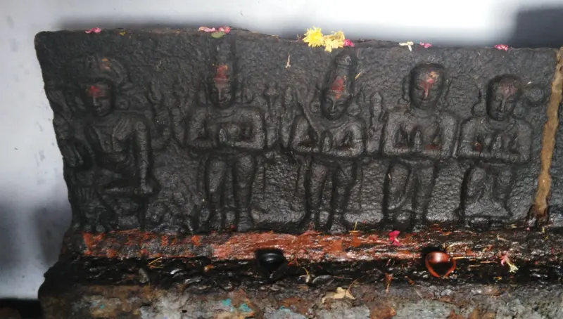 A stone relief of five figures with folded hands, marked with red powder