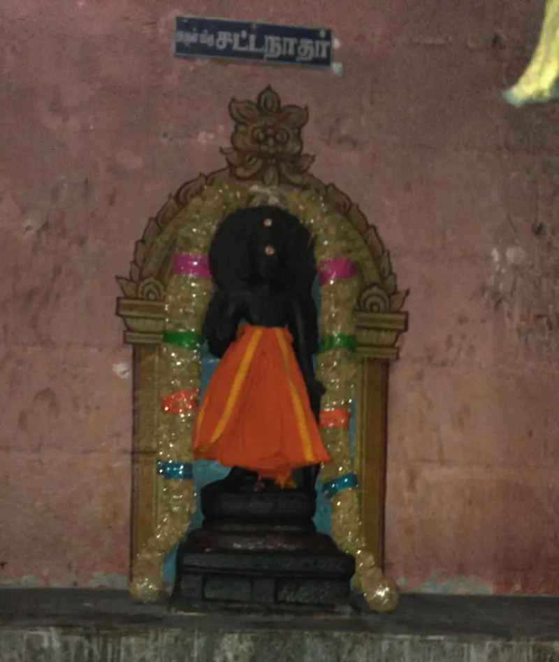 A black stone figure in an orange cloth under a flower-garlanded arch