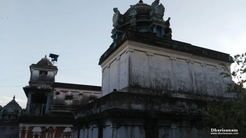 A whitewashed shrine block with a dark domed top and corner figures rises above a lower stone wall