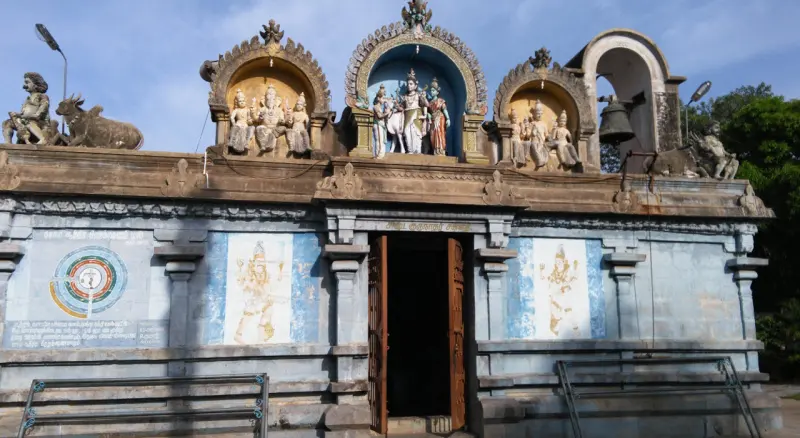 Front of a blue-grey temple hall with an open wooden door and painted stucco figures on the roof