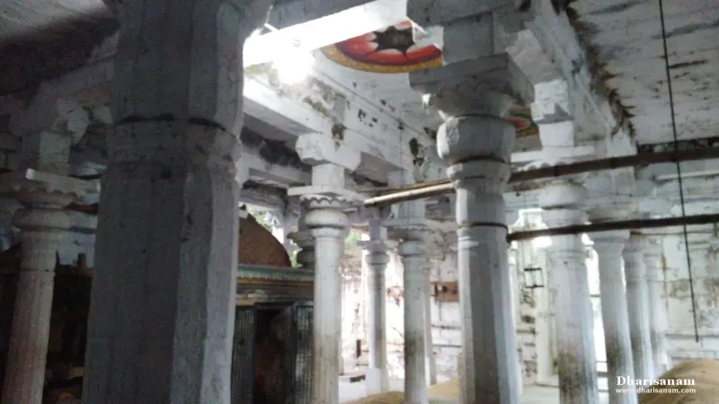 Rows of whitewashed stone pillars in a hall with a painted ceiling panel and a small shrine beyond