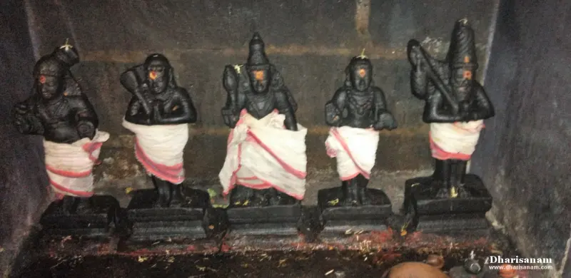 Five small black stone idols wearing white cloth with red borders, standing on low bases