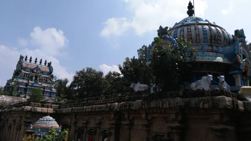 Stone wall with white bull figures along its top, a domed shrine roof, and a tower in the distance