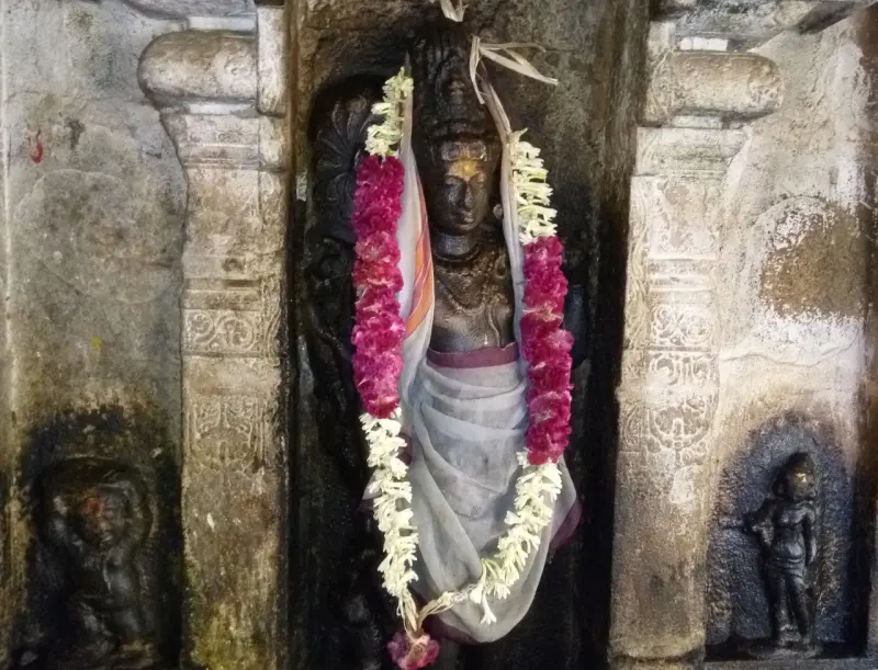 Dark image wearing flower garlands and a white cloth, in a niche between carved pillars