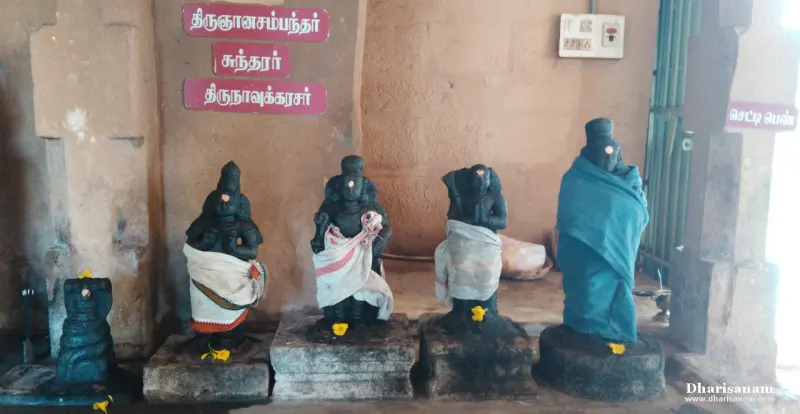 Four black stone figures in a row on stone bases, with Tamil name boards on the wall behind