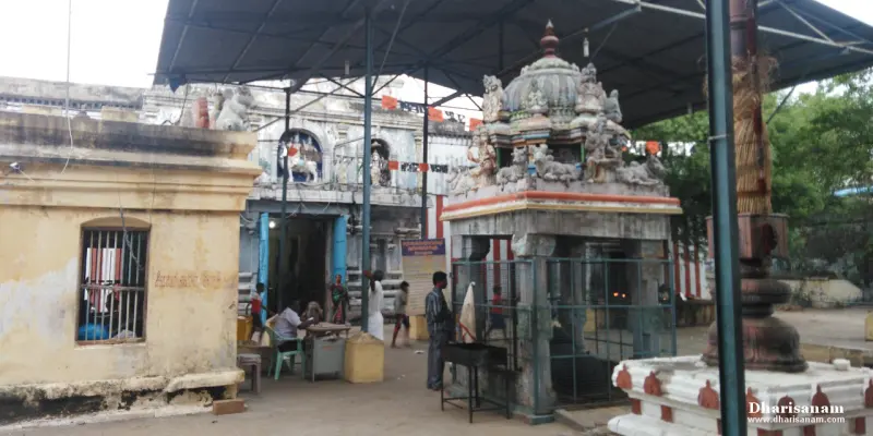 A small shrine with a carved tower stands under a metal roof beside a paved courtyard.