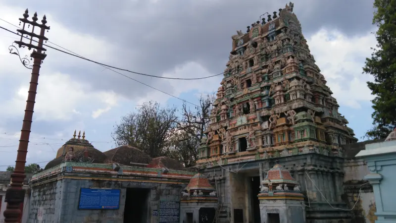 Tiered gopuram with many figures, beside a tall flagstaff, under a cloudy sky