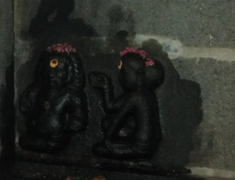A dark relief of two seated figures facing each other, each wearing a pink garland on the head