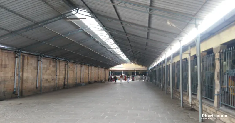 A long corridor under a sloping metal roof, stone wall at left and railings at right